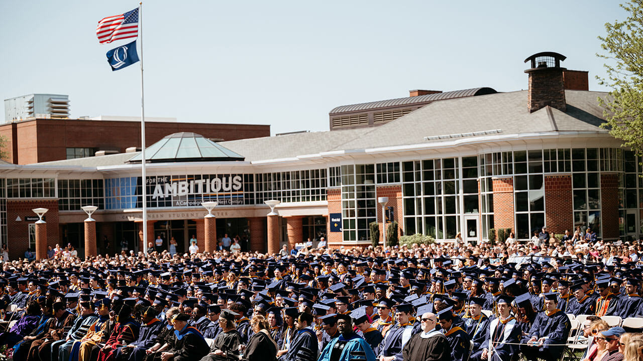 A wide photo of Quinnipiac graduates sitting on the quad