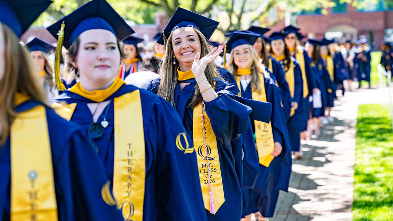 A graduate in the procession line waving into the distance