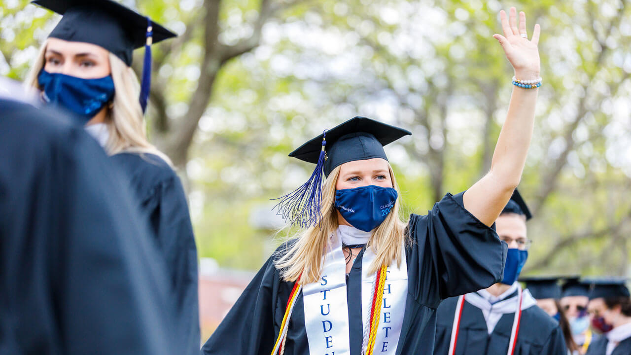 Graduate walking into commencement and waving at family
