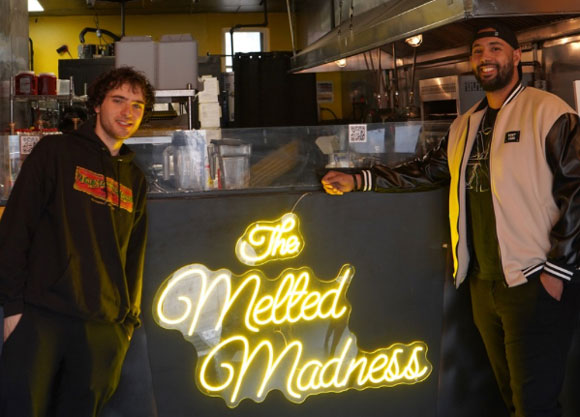 Dj Ford smiling in front of a sign that reads "The Melted Madness"