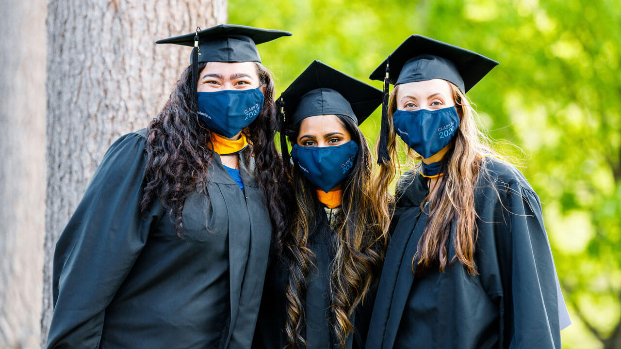 A group of three graduates posing for photo wearing their cap and gowns