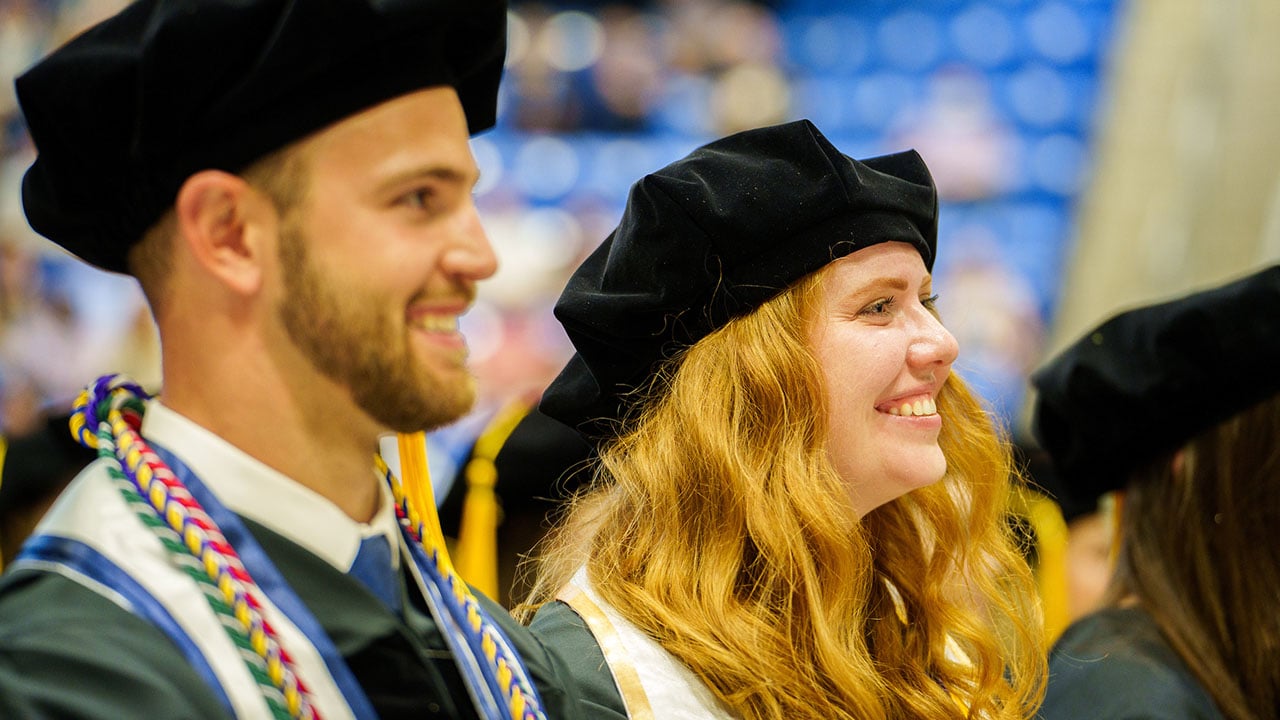 Two graduates in their seats smiling at the stage