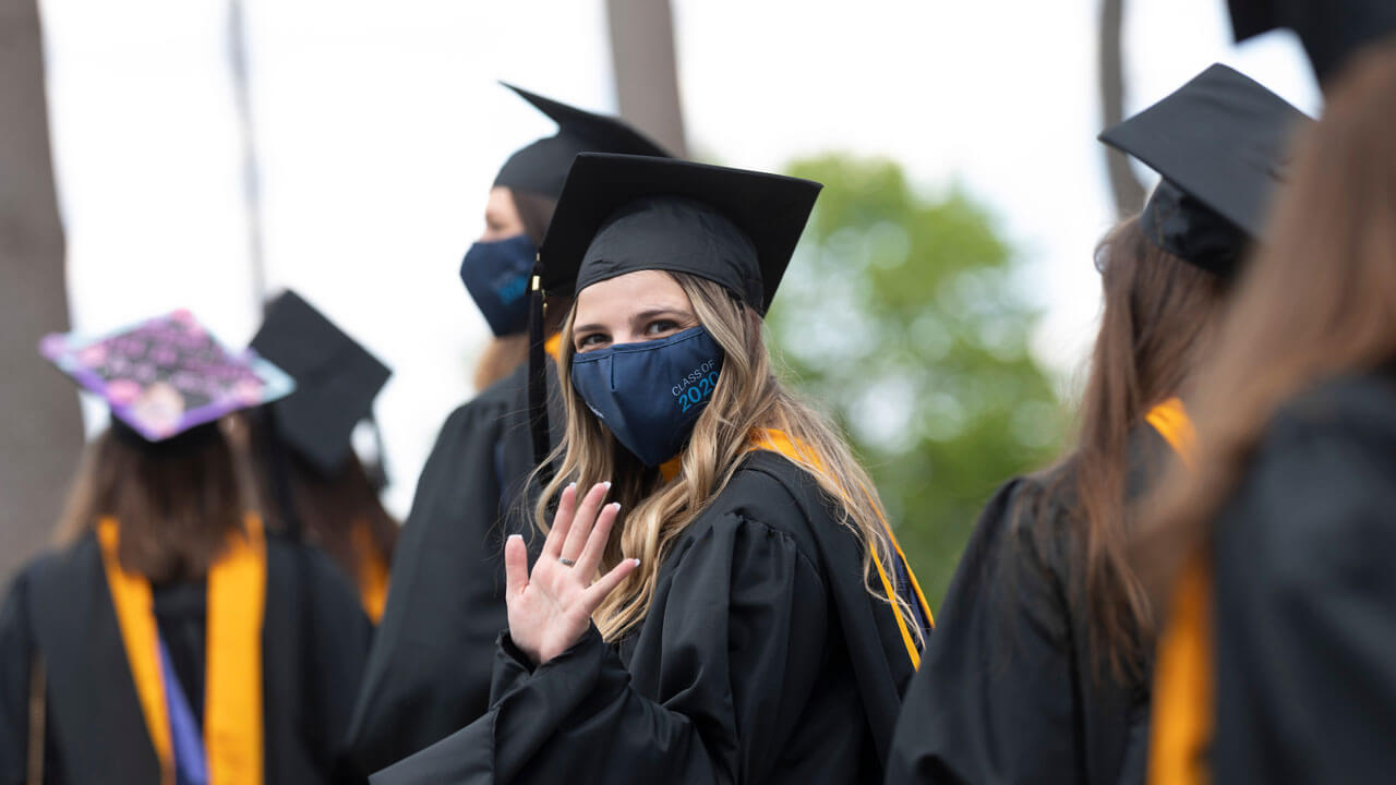 Graduate waving at the camera in the pine grove