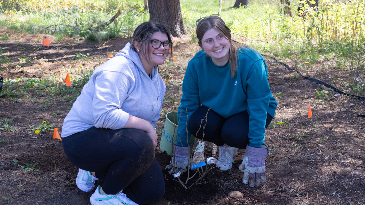 Two Quinnipiac students kneeling in dirt smiling