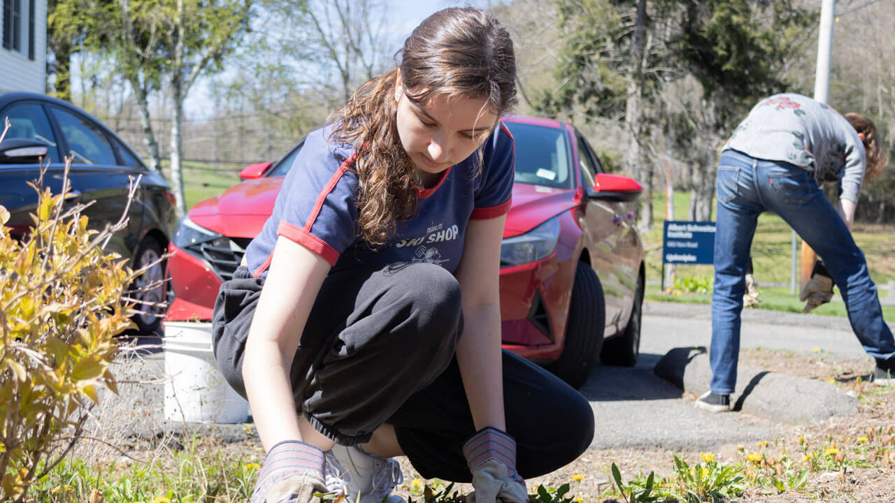 Quinnipiac Arbor Day student wearing gloves to weed