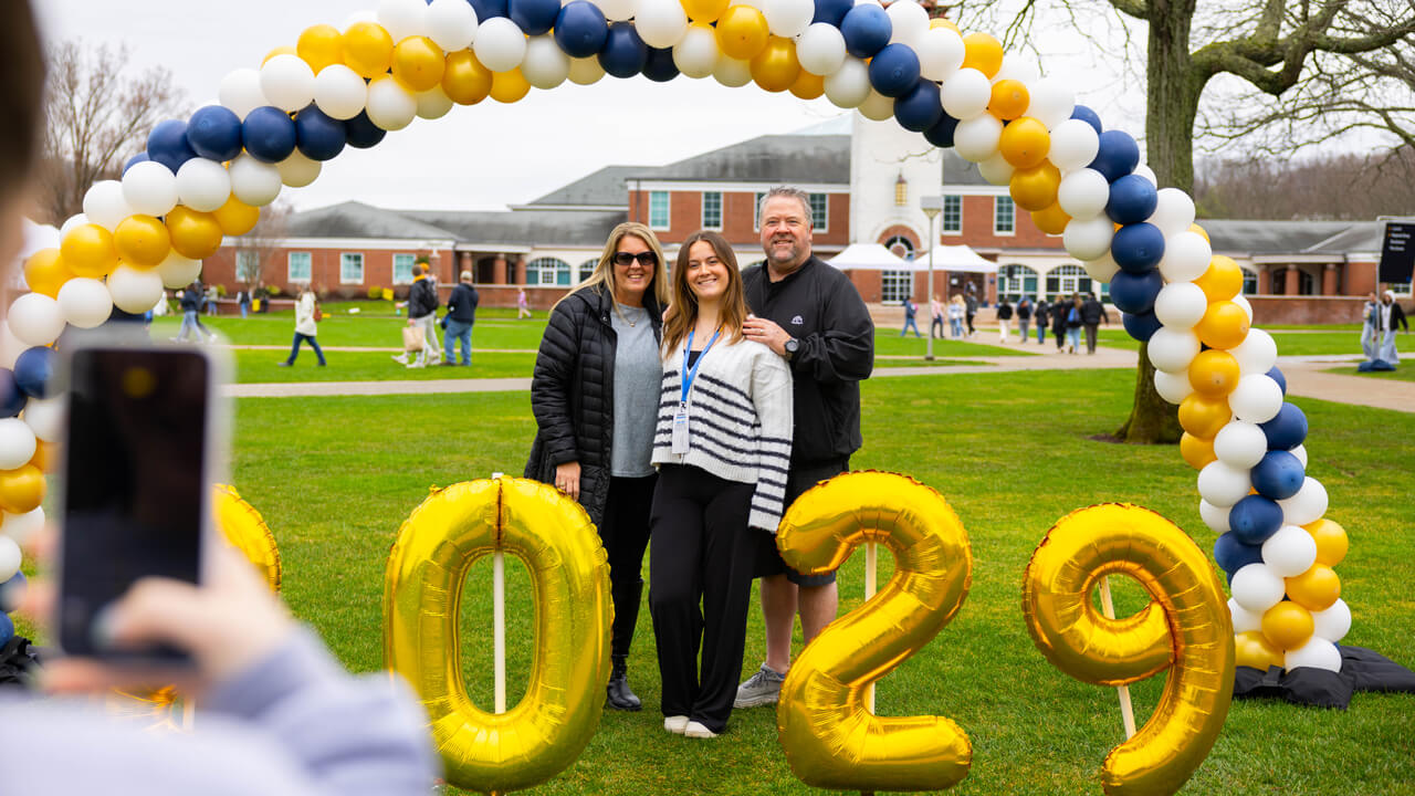 A student and loved ones pose in front of the library under a balloon arch and 2029 balloons