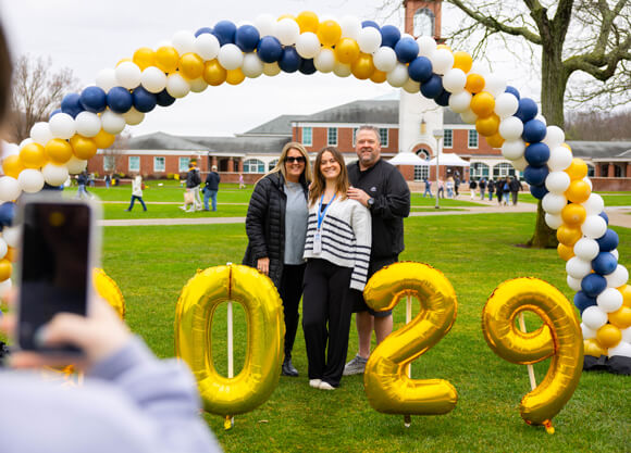 A student and loved ones pose in front of the library under a balloon arch and 2029 balloons
