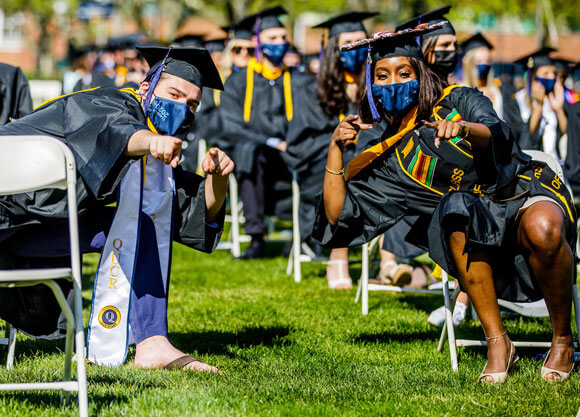 Two graduates lean in an give a thumbs up from their seats