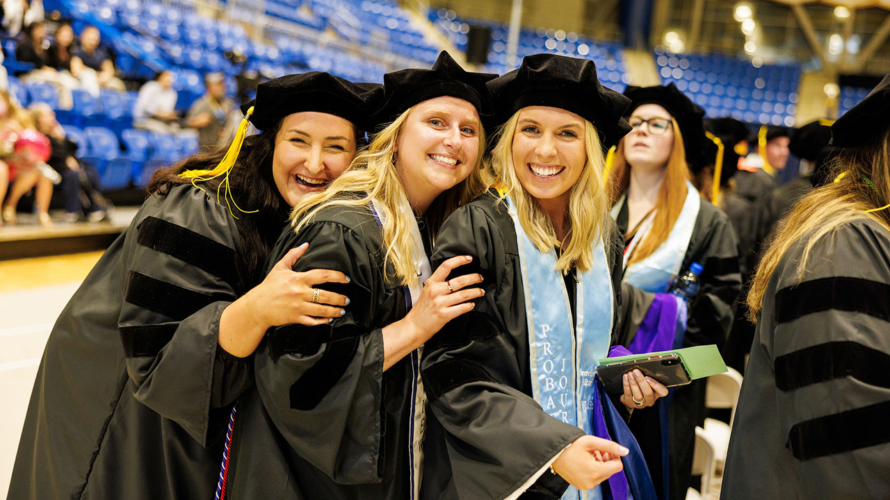 Three graduates group together and smile