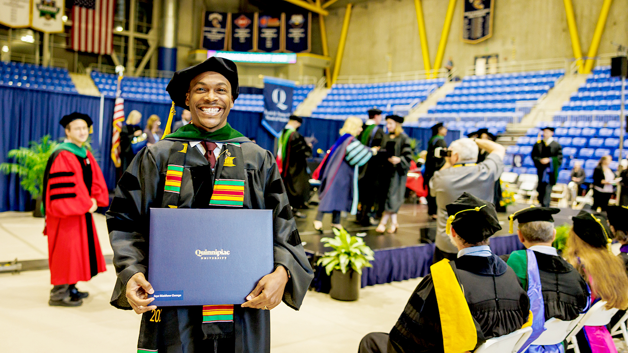 A graduate holds up their diploma offstage and smiles