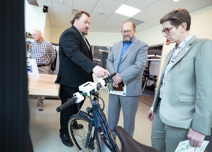 A student shows a bicycle-based engineering project to faculty members in a lab during Projects Day.