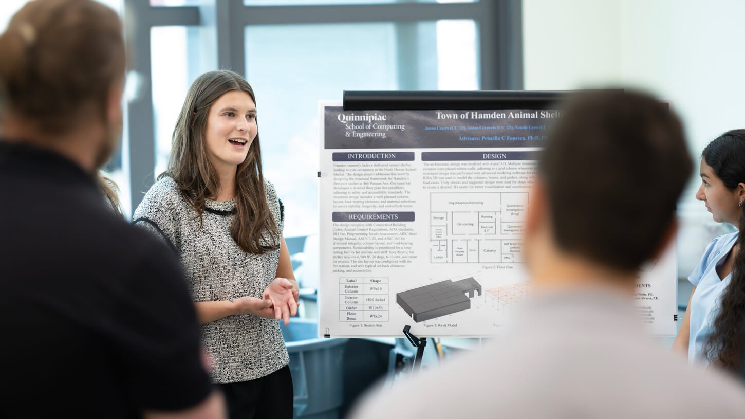 A student enthusiastically presents a proposal for the Town of Hamden Animal Shelter while peers and faculty gather around.