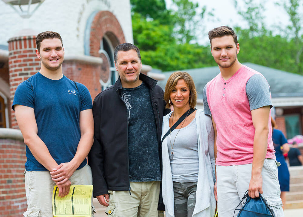 Two parents pose in front of the Arnold Bernhard Library with their two students by their side