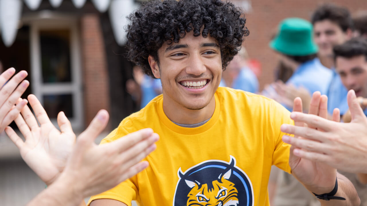 A new student in a gold Quinnipiac shirt smiles and gives high fives
