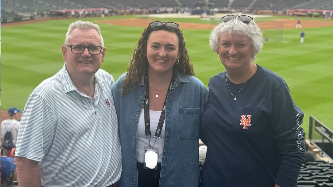 Three people smile for a photo in a baseball stadium.