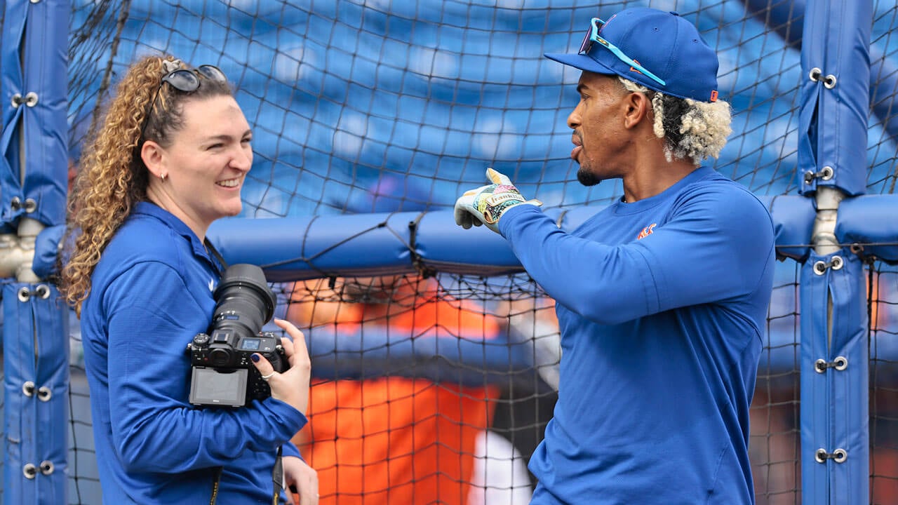 Photographer smiles and talks with a baseball player.