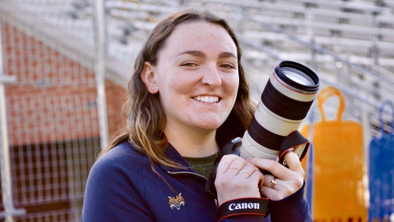 Photographer smiles while holding up a camera.