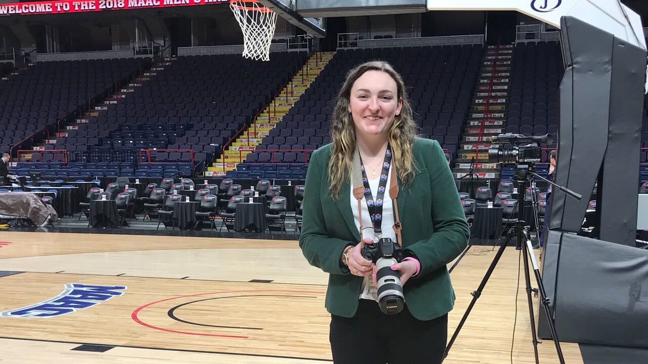 Photographer smiles for a photo with a basketball court in the background.