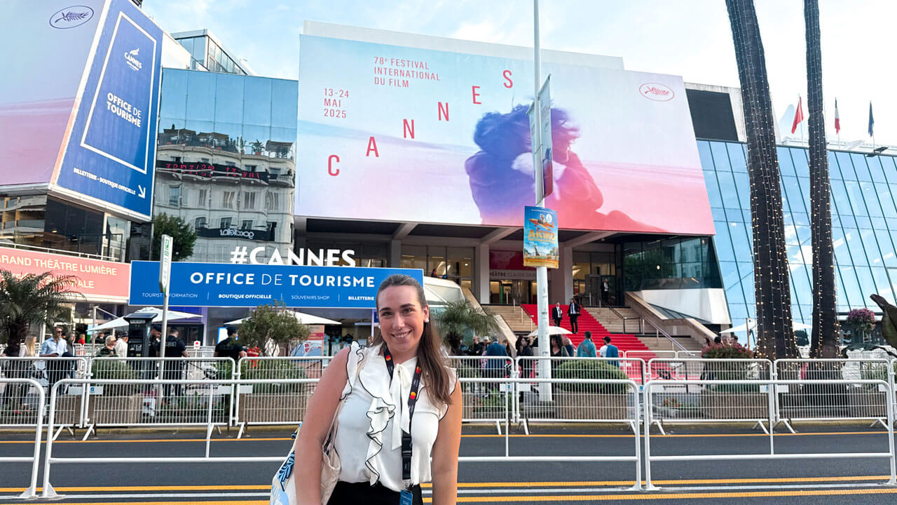 Individual stands in front of the Cannes Film Festival banner and red carpet.