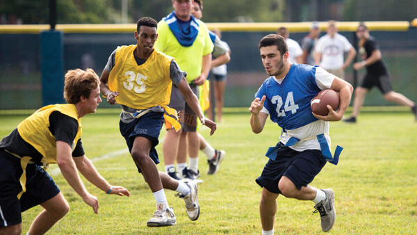 Graduate student Jared Einhorn runs with a football toward two other flag football players