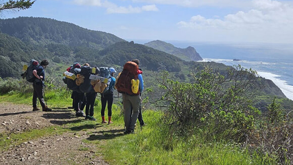 Students look out at a view of the ocean at the summit of a hike