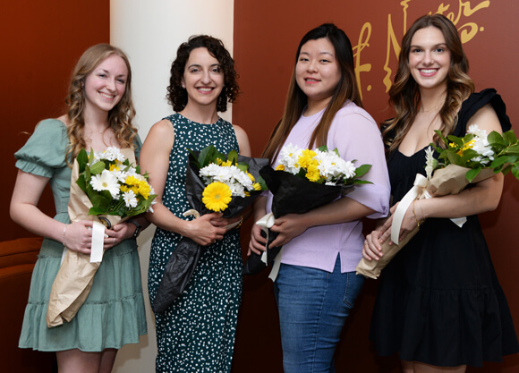 Four people pose holding bouquets of daisies