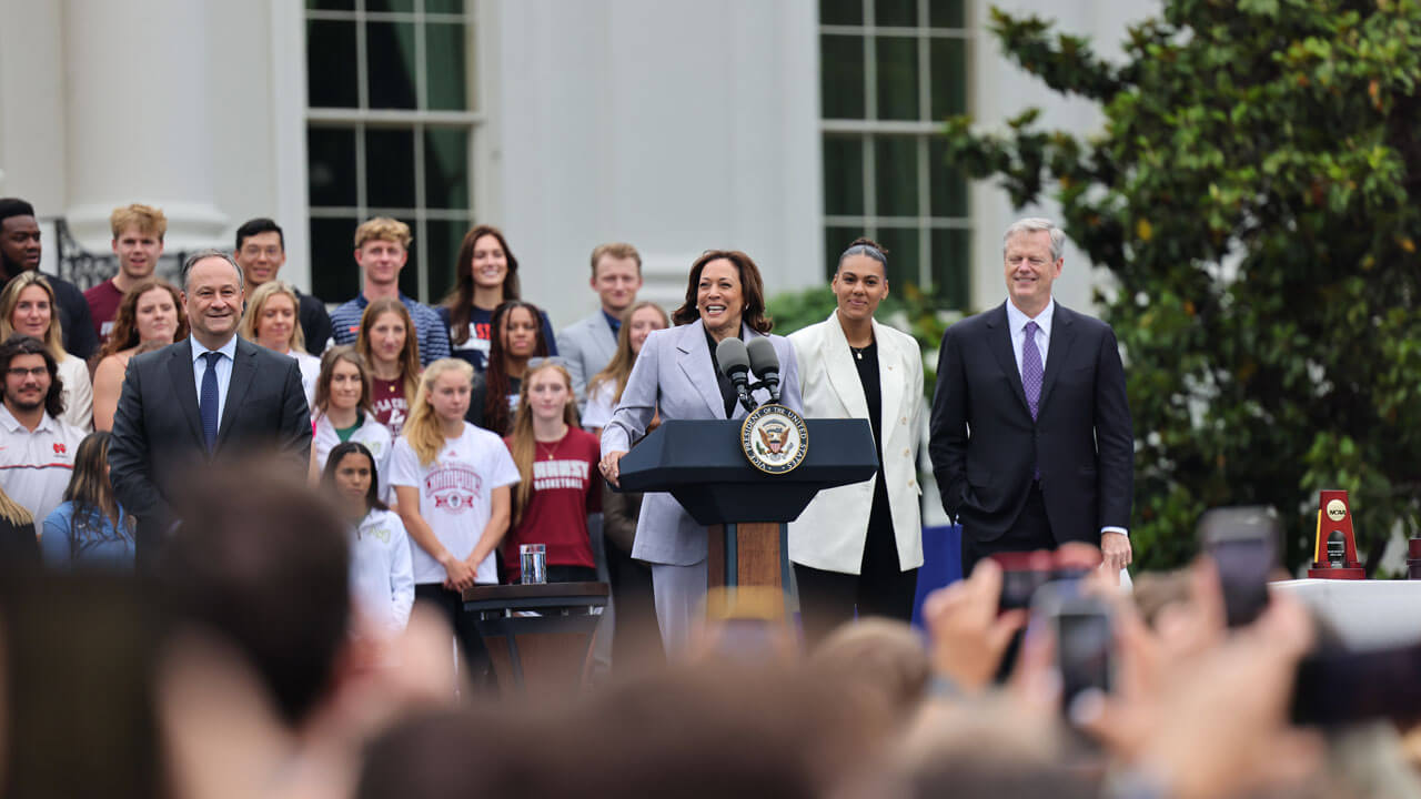 Kamala Harris speaking to audience with Quinnipiac Hockey team behind her