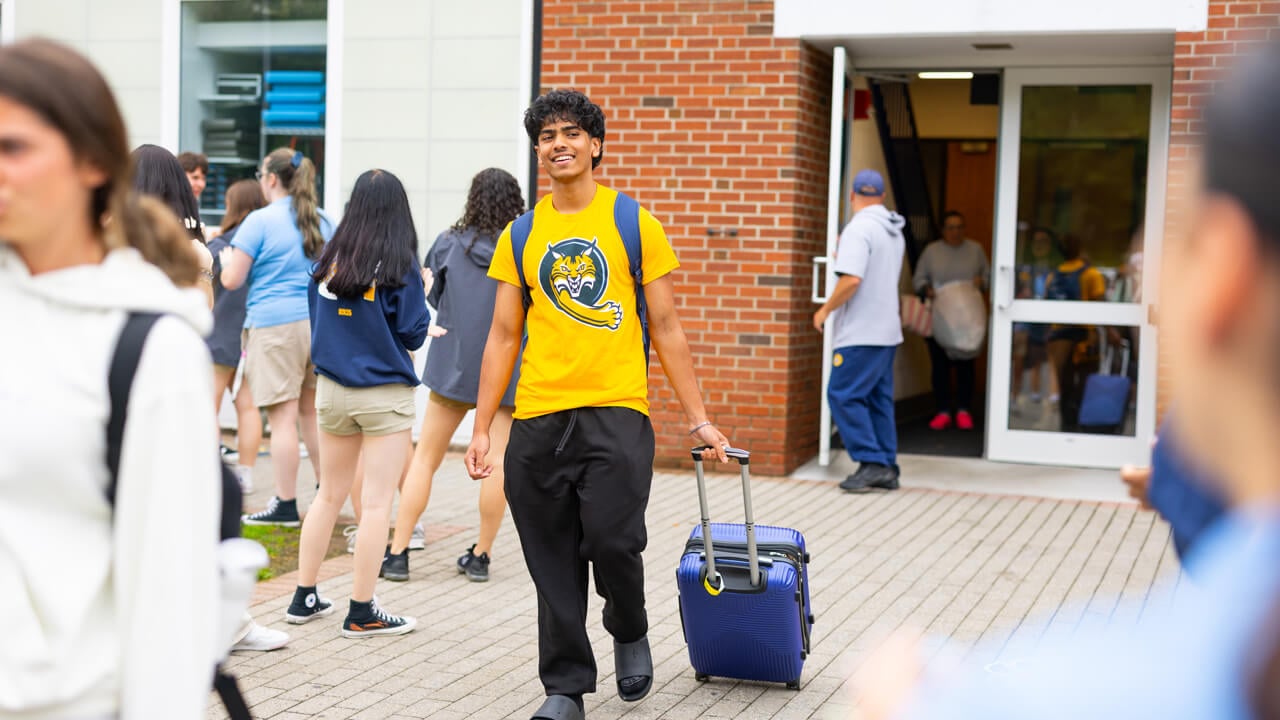 Individual walking out of the Recreation and Wellness Center with a blue suitcase