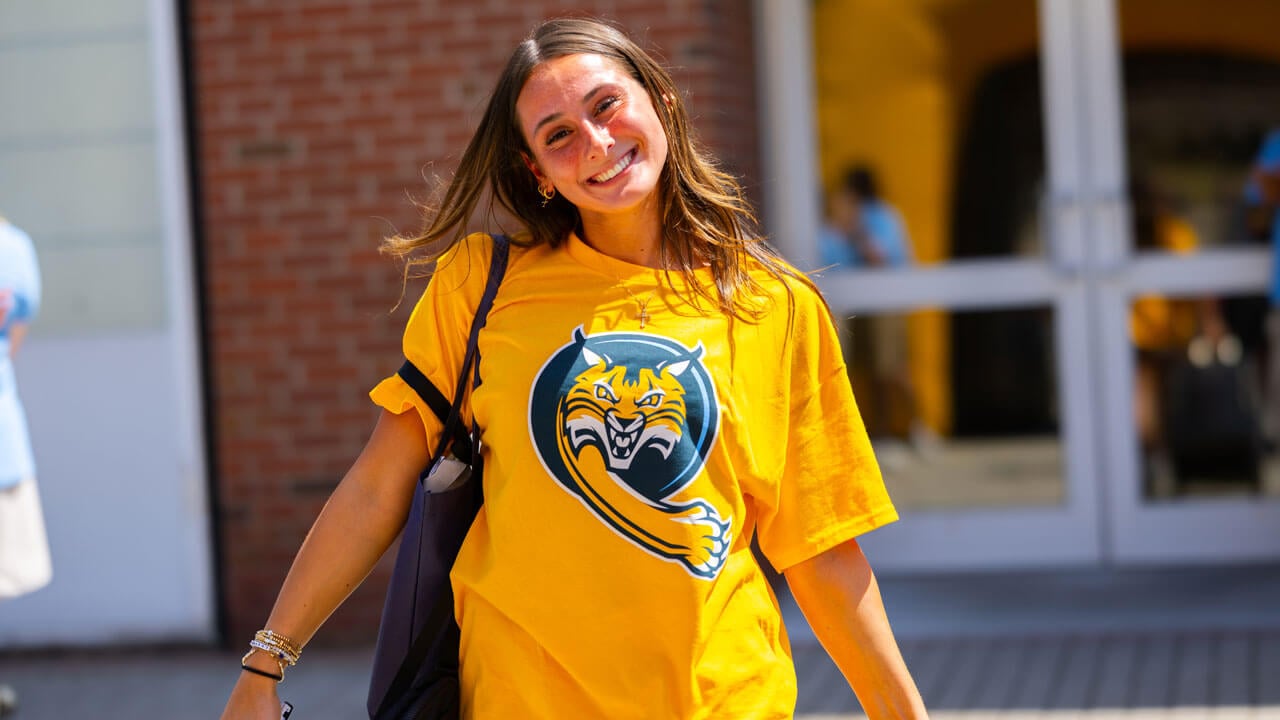 Individual smiles at the camera for a photo in front of the Recreation and Wellness Center.