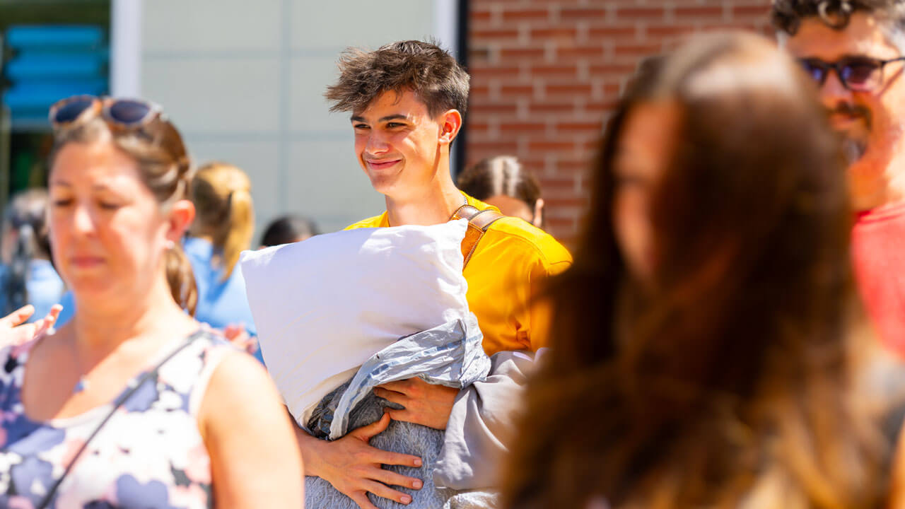 Individuals walks carrying a pillow.