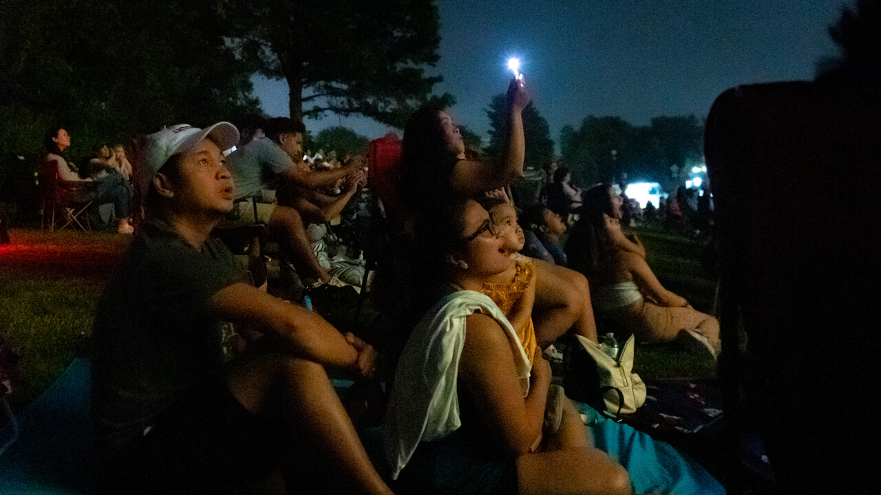 A small child and family members smile in awe in the twilight on the Hamden green