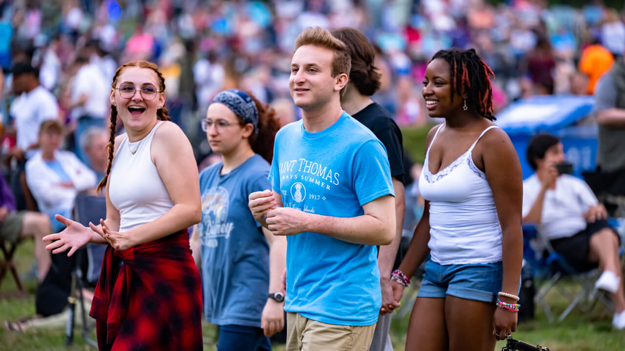 Teenagers walk on the Hamden green with hundreds of firework attendees in the background