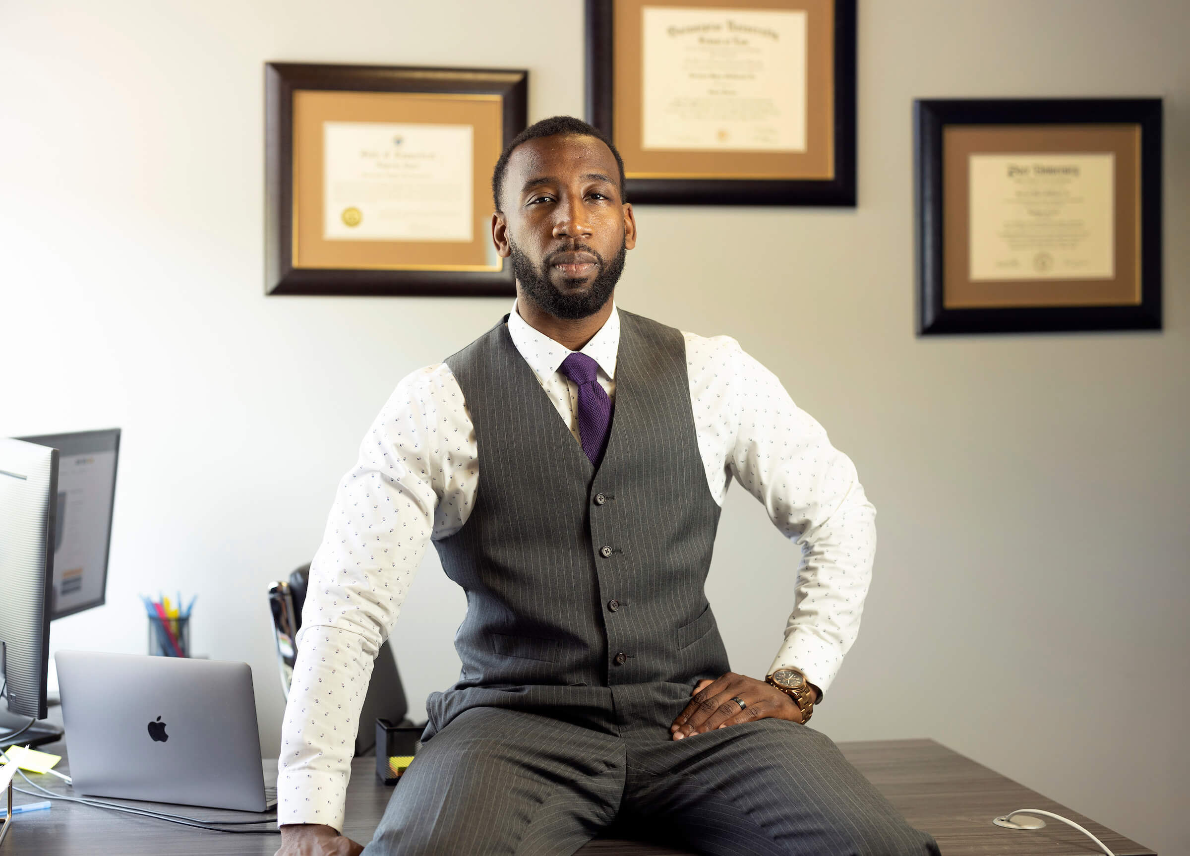Bert McDowell sitting on his desk with his diplomas behind him