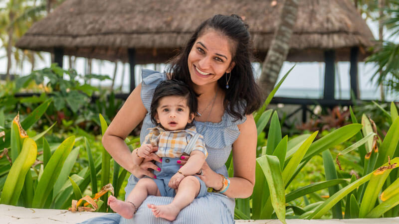 Baby Kumar is held by his mom in front of several palm trees