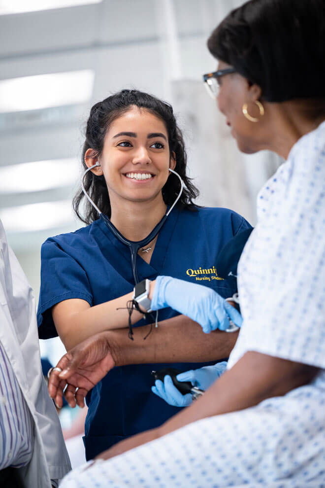 A nursing student smiles while helping a patient.