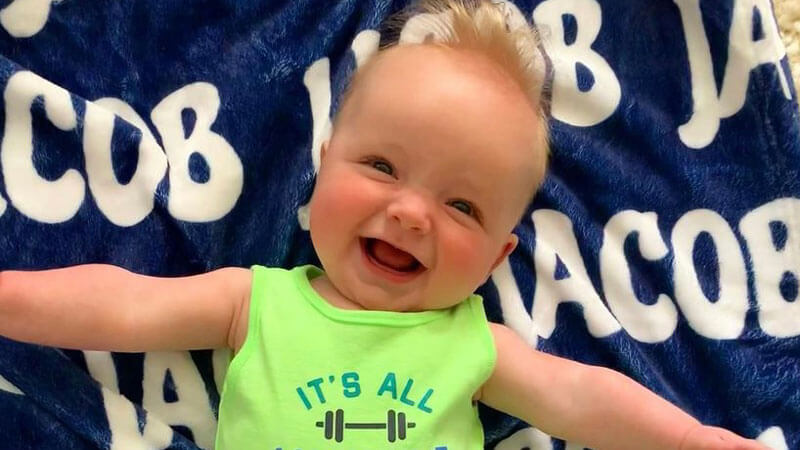 Jacob Sirois smiles broadly as he lays on a blanket with his name