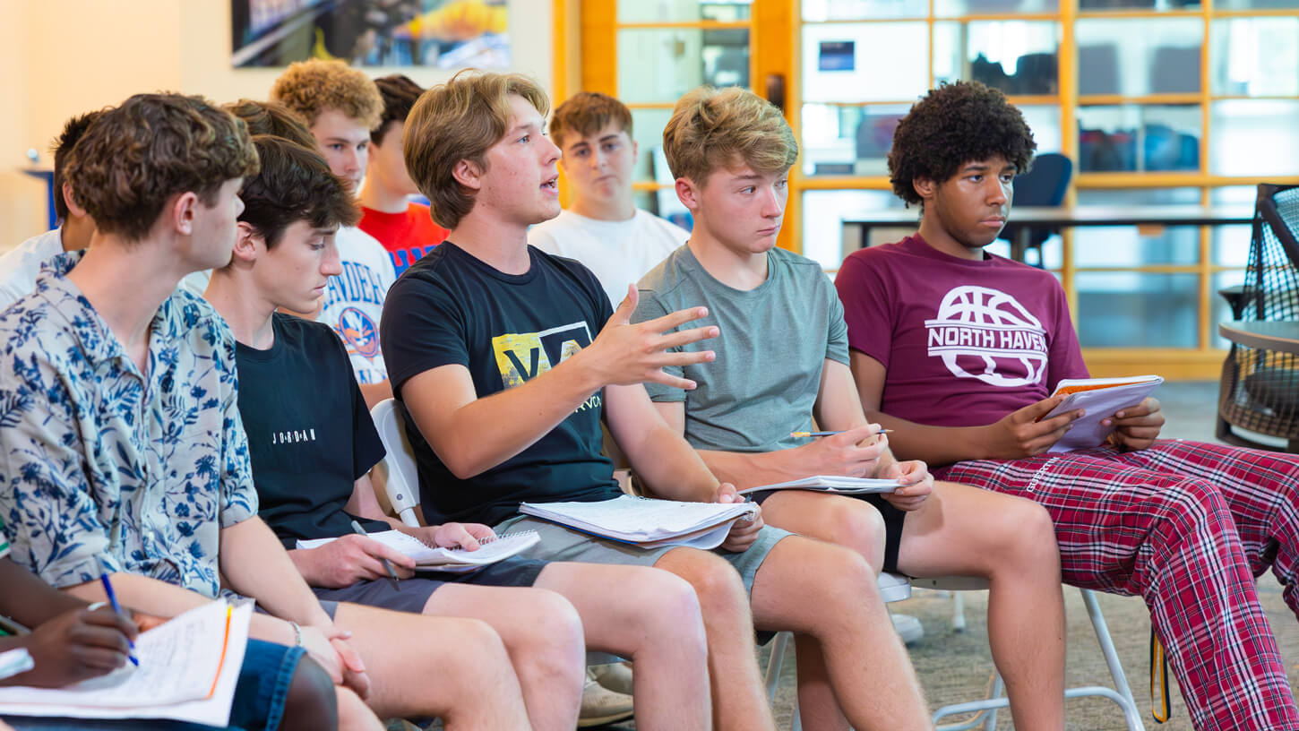 Group of high school students seated indoors, attentively discussing and taking notes during a session at Quinnipiac University’s Sports Communications Summer Camp.