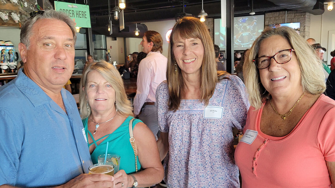 Four alumni smile for a photo while enjoying a drink at Stony Creek Brewery in Branford, Connecticut