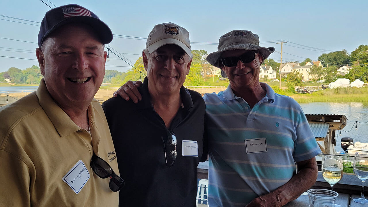 Three men smile for a photo by the water