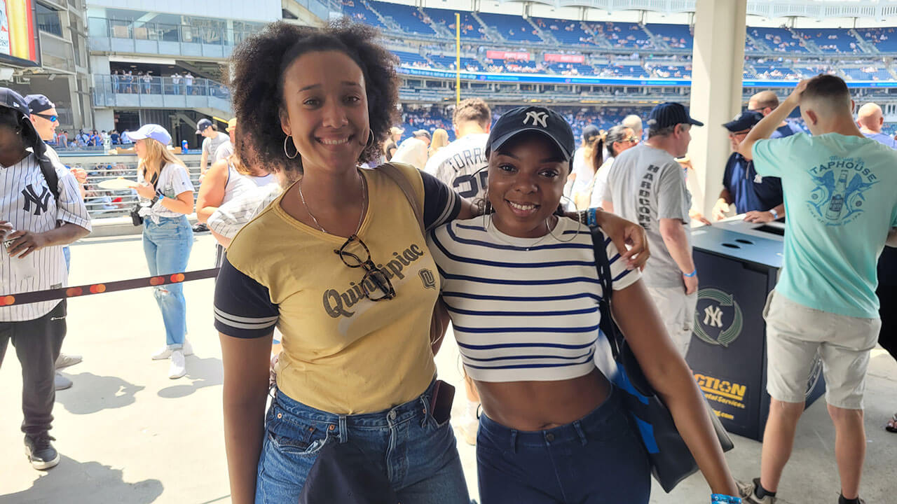 Two alumnae members take a photo in front of a baseball field