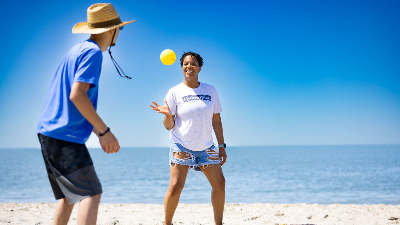 Students play spike ball on the beach with vibrant and clear blue skies