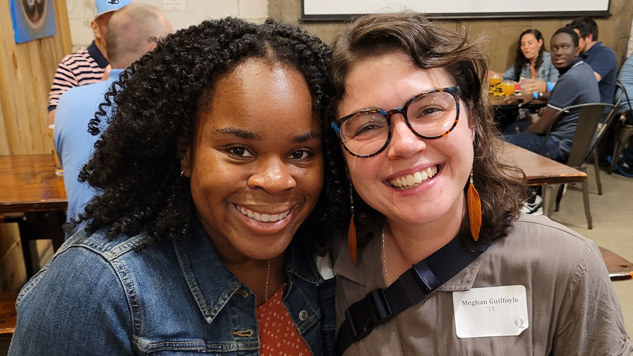 Two alumnae smile for a photo at a happy hour