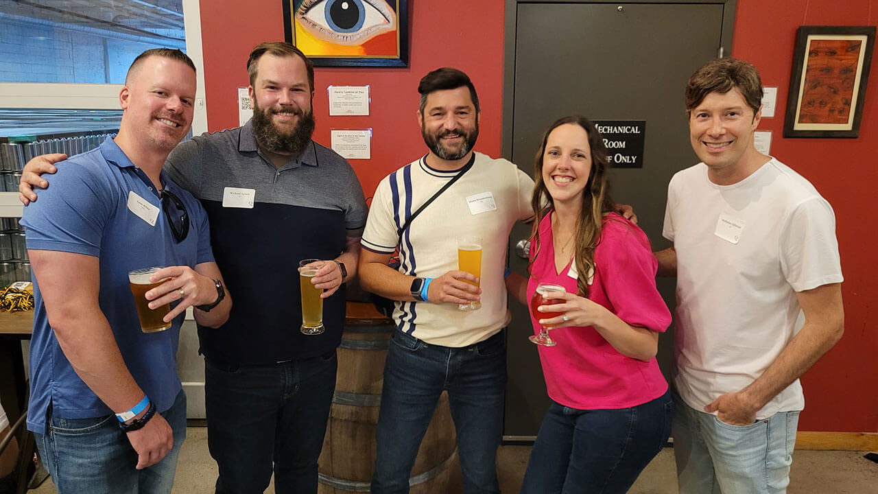 Alumni pause for a photo with drinks in their hands