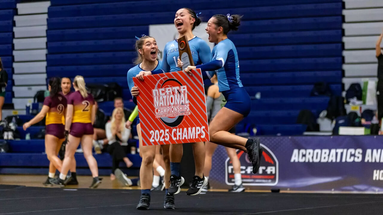 Acrobatics and tumbling athletes cheer and hug with a 2025 championship sign