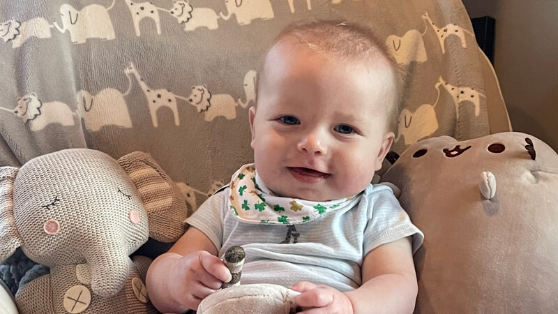 Baby Bobriwnyk smiles as he sits in an armchair with stuffed animals