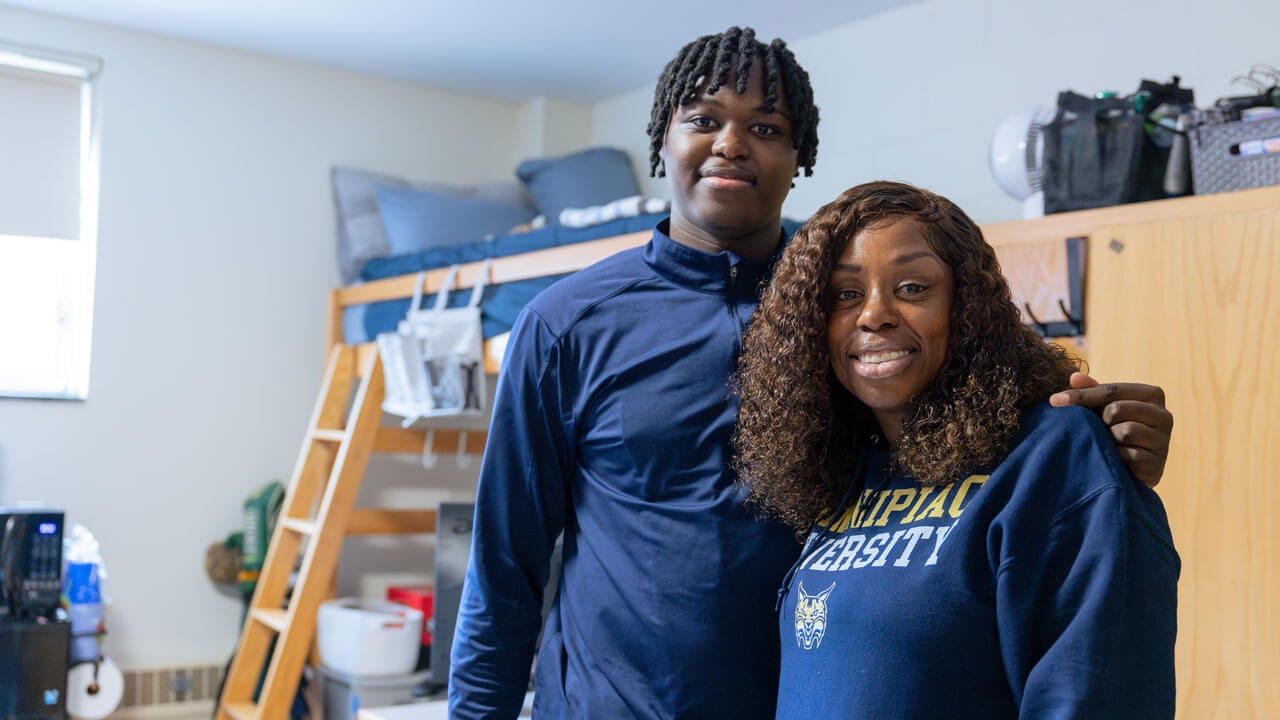 A student and their loved one smile in their dorm.
