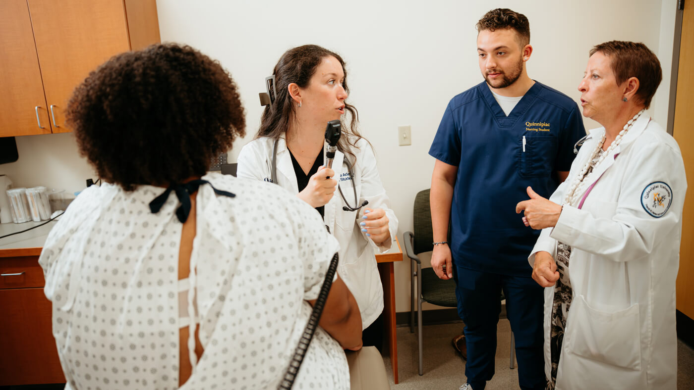 Nursing students being observed by a faculty member as they perform a physical exam on a standardized patient.