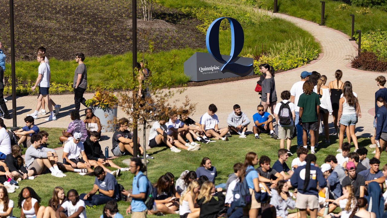 Students sit on South Quad lawn with a navy Q sign in the background