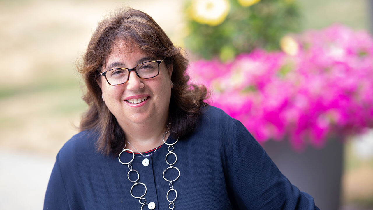 Lisa Rebeschi smiles outside with flowers in the background