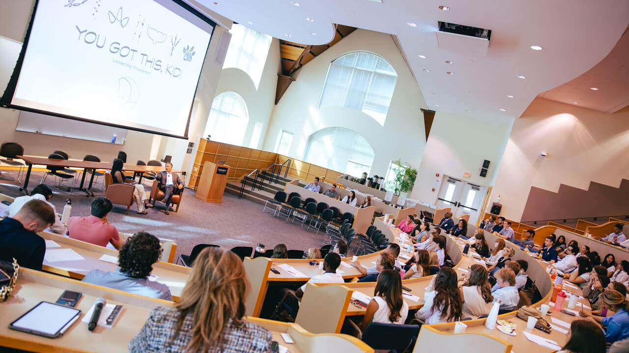 Visual of students sitting in auditorium and of guest speakers